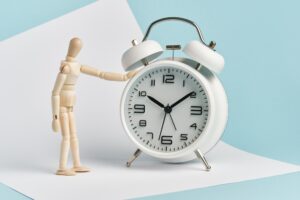 Wooden man stands with his hand on the alarm clock. Time management, waiting, punctuality.