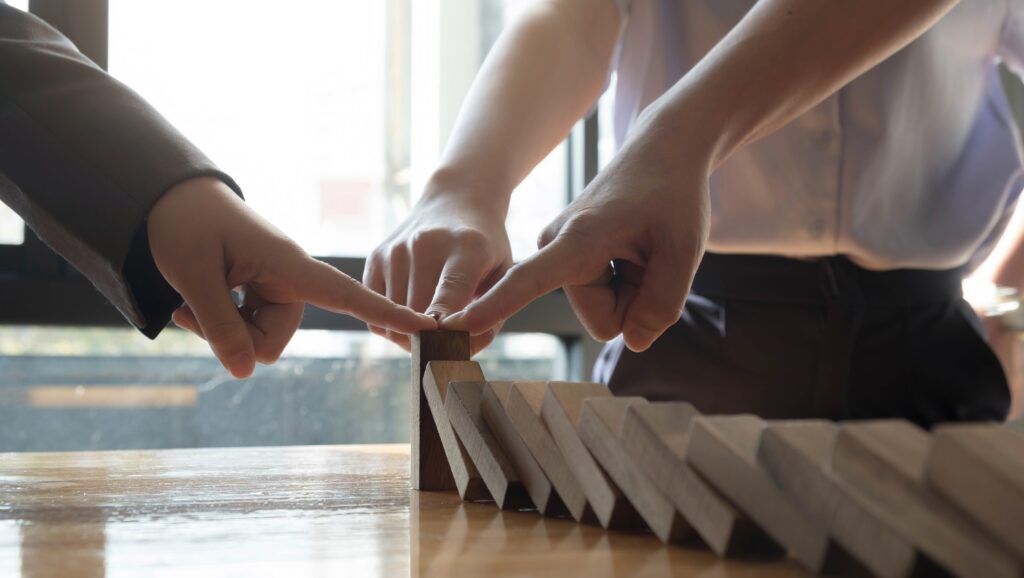 close up team businessman hand stopping falling wooden dominoes effect from continuous toppled or